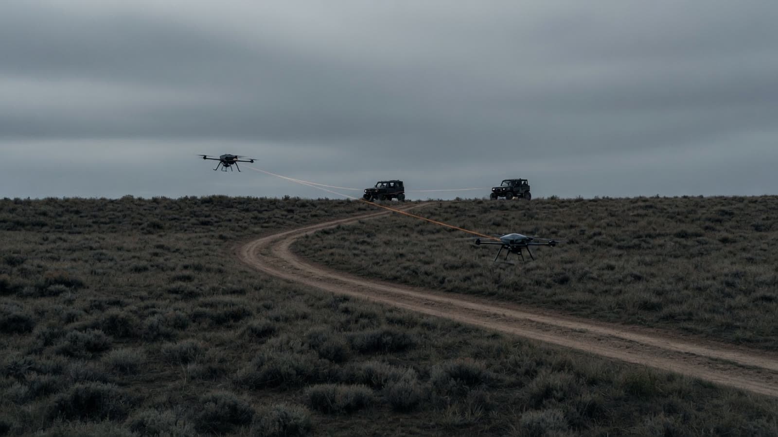 Two small quadcopters over a dirt track at dusk, with faint links back to vehicles on a ridge. Conceptual.